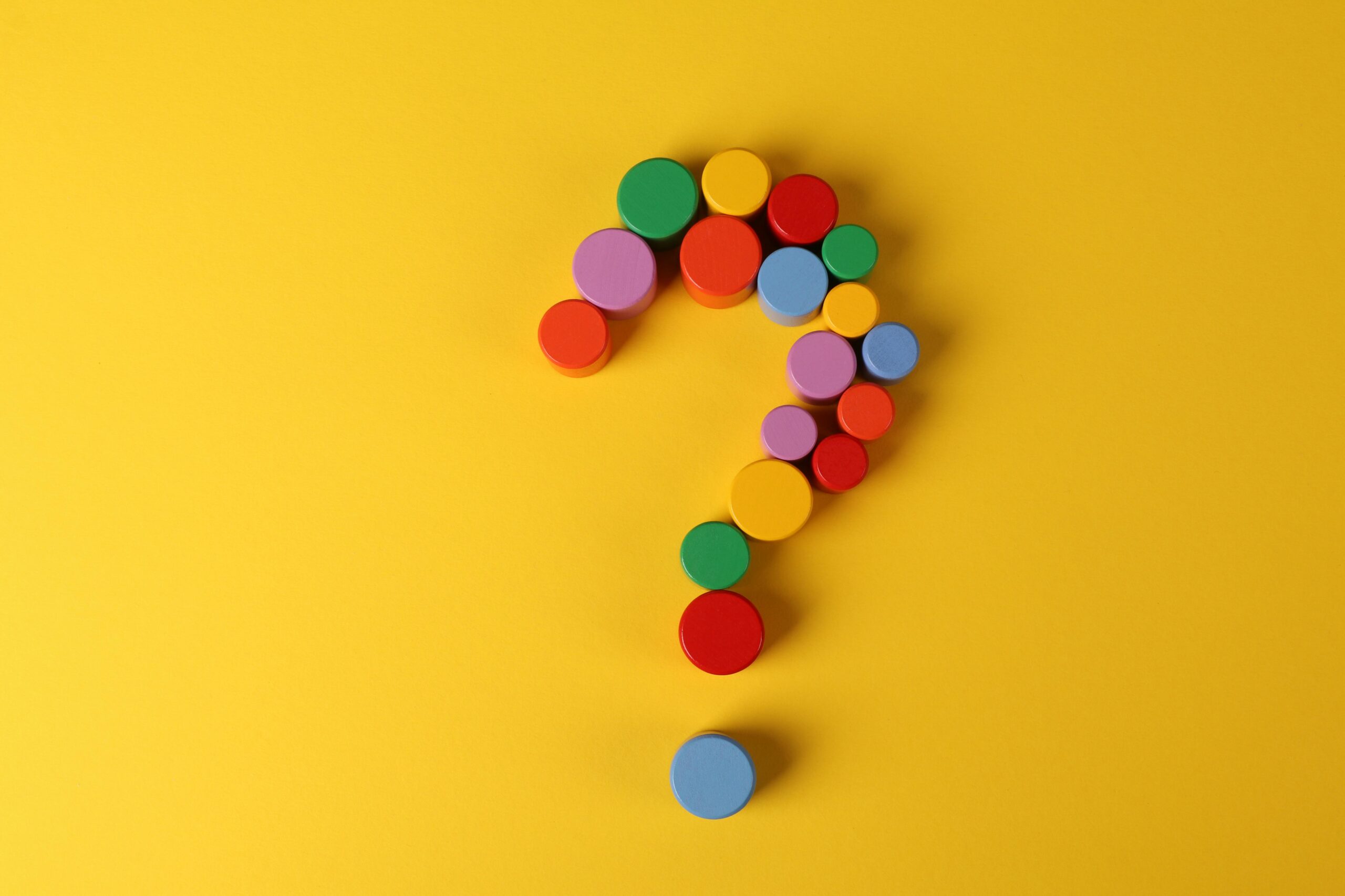 A vibrant question mark made from colorful circular blocks on a yellow background, symbolizing curiosity and inquiry.